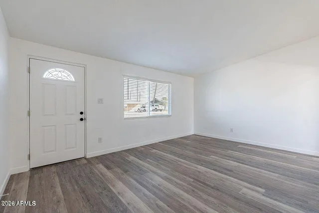 a view of an empty room with wooden floor and a window
