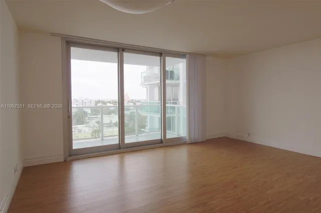 a view of an empty room with wooden floor and kitchen