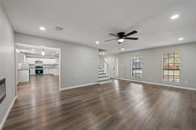 a view of an empty room with wooden floor and a kitchen