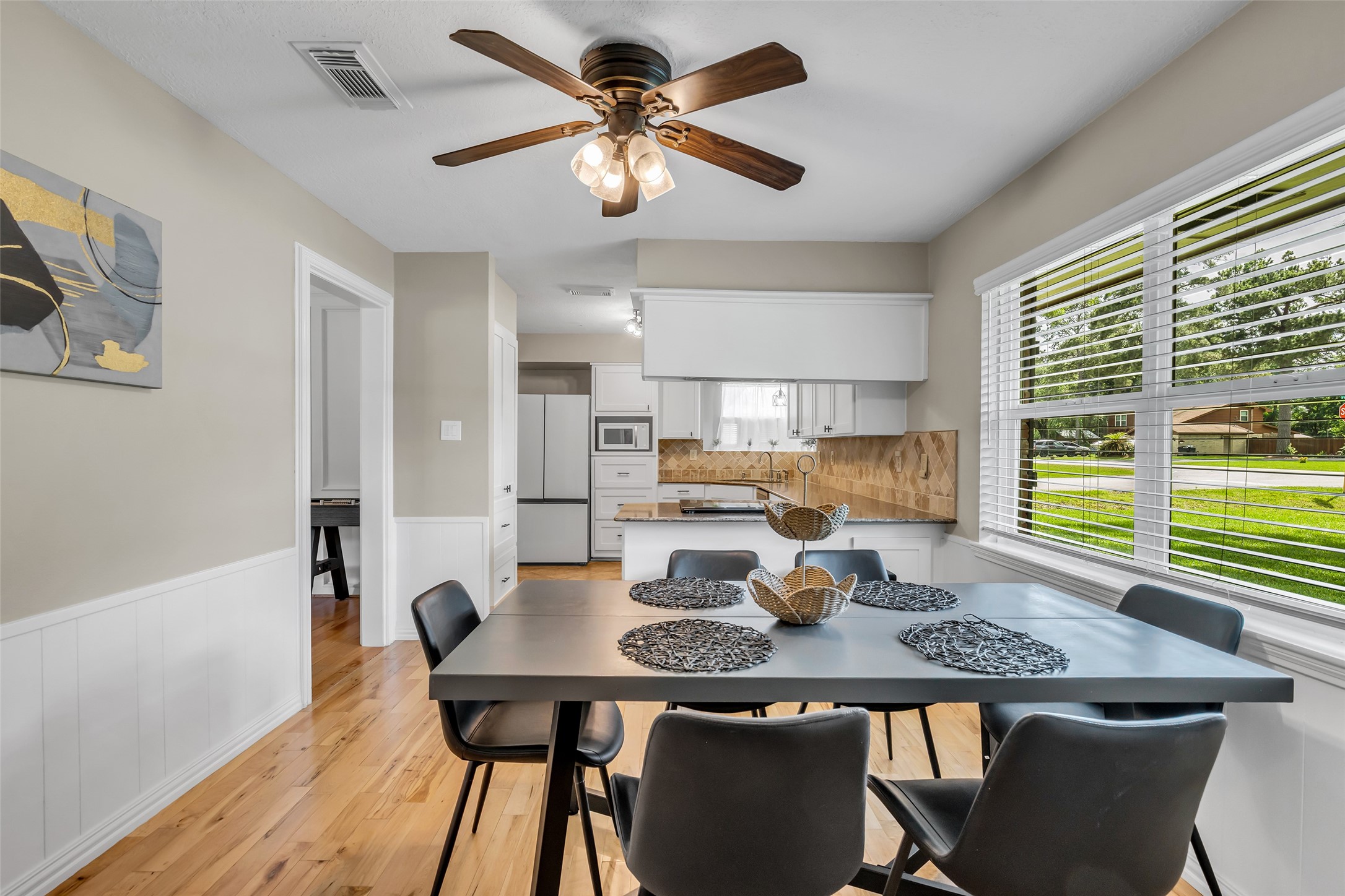 22502 Fields Lane Spring, TX 77389 - Photo 9 of 39 Bright dining area with hardwood floors. Large windows provide natural light and a view of the green lawn. The open layout leads to a well-lit kitchen with white cabinetry.