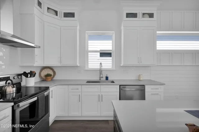 a kitchen with stainless steel appliances granite countertop white cabinets a sink a stove and a window