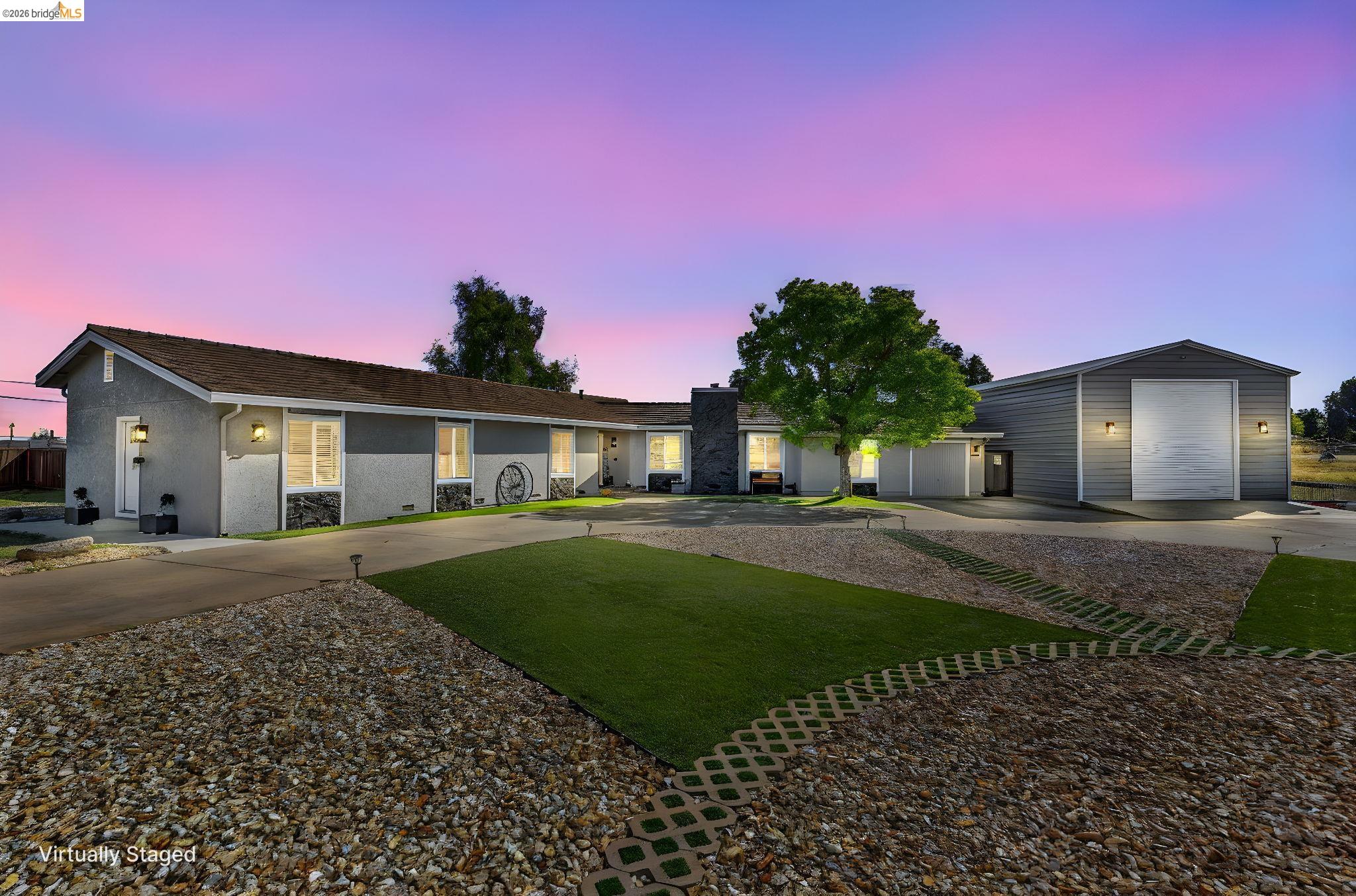 Exterior featuring a gravel driveway, artificial turf accents, and a detached metal building with a roll-up door