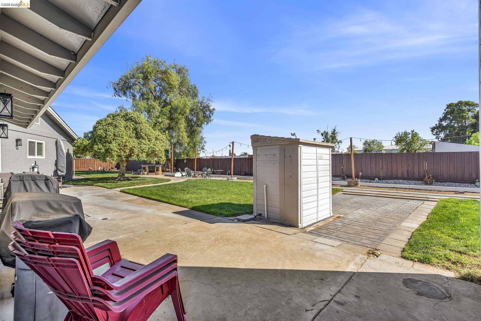 59 Old Stagecoach Road Brentwood, CA 94513 - Photo 50 of 70 Expansive concrete patio area with a covered section, bordered by a large grassy lawn, a storage shed, and a privacy fence