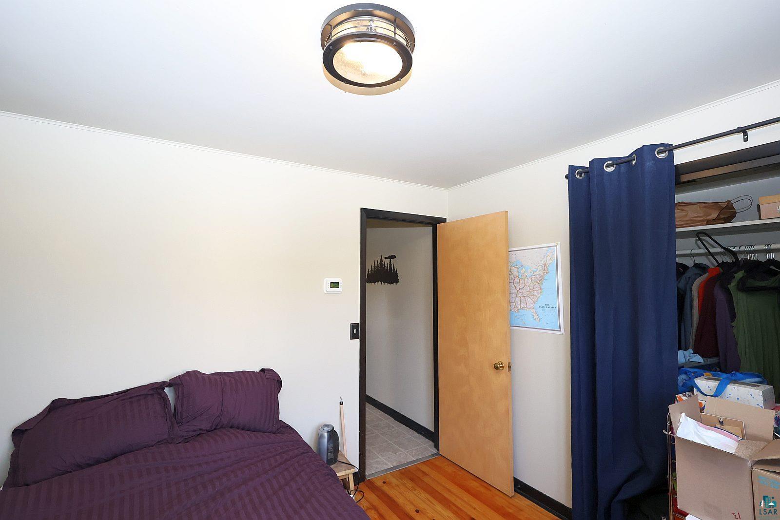 83185 Washington Avenue Port Wing, WI 54865 - Photo 16 of 26 Room featuring light-toned walls, wood-finish flooring, a flush-mount ceiling light fixture, a solid core door with a metal knob, and a closet area with an overhead shelf and clothing rod