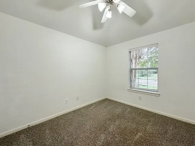 an empty room with a chandelier fan and windows
