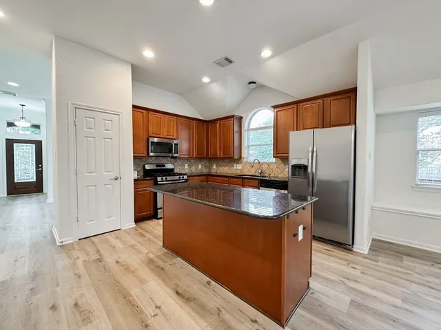 a kitchen with stainless steel appliances granite countertop a refrigerator a stove top oven a sink and dishwasher with wooden floor