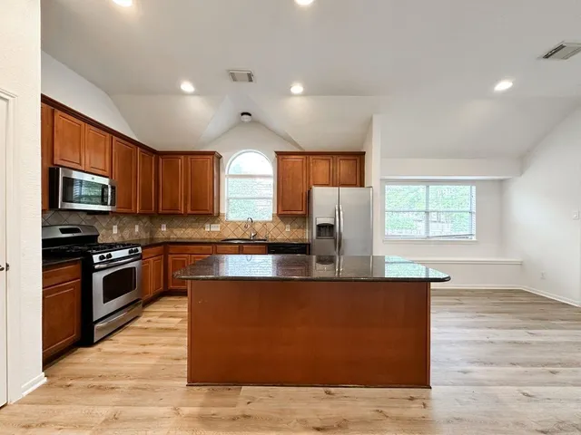 a large kitchen with stainless steel appliances granite countertop a stove a sink dishwasher and a microwave oven with wooden floor