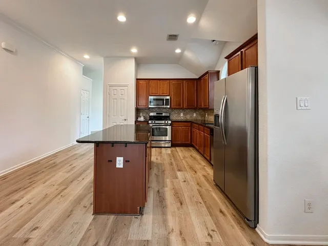 a kitchen with stainless steel appliances granite countertop a refrigerator a stove and a wooden floors