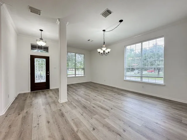 an empty room with wooden floor chandelier and windows