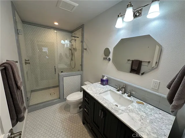 a bathroom with a granite countertop sink a toilet a mirror a vanity and shower