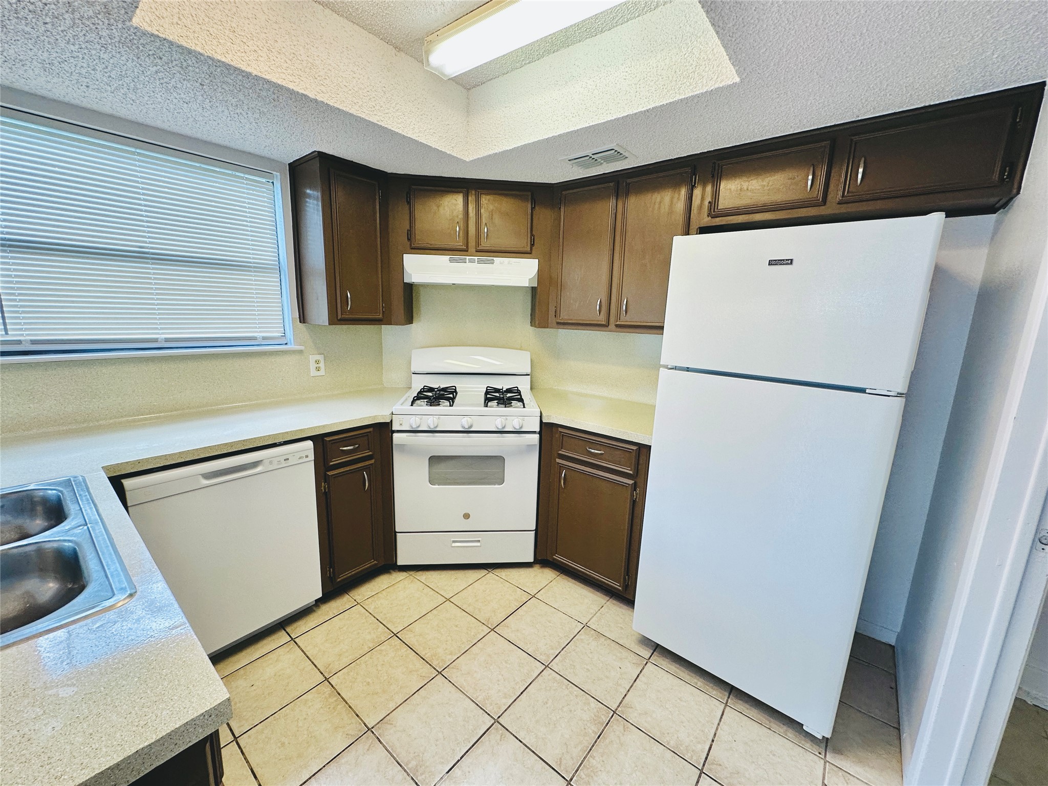 1002 Ridgemont Street Round Rock, TX 78664 - Photo 11 of 30 Kitchen featuring white appliances, light countertops, a textured ceiling, light tile patterned floors, and dark brown cabinets