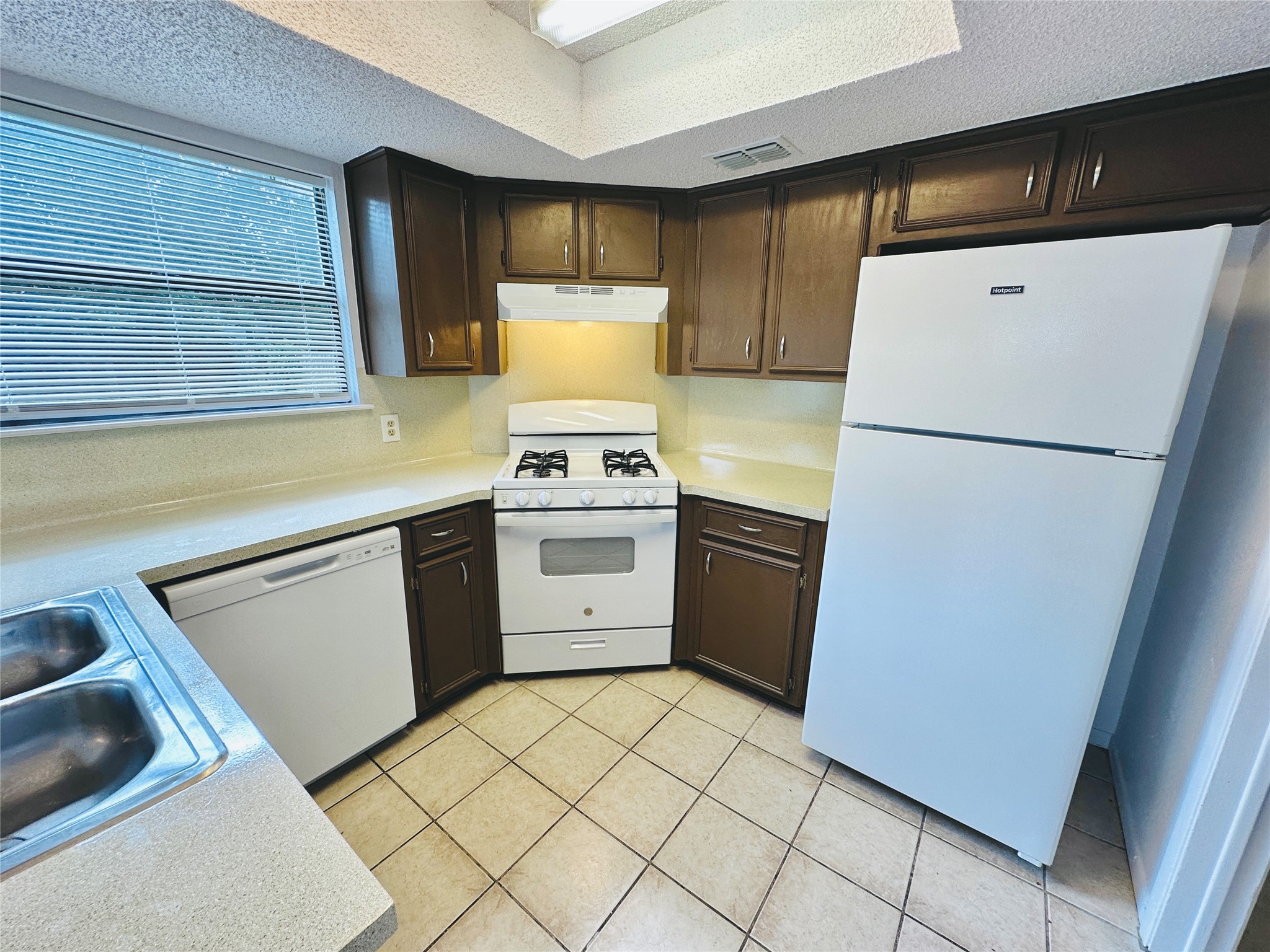 1002 Ridgemont Street Round Rock, TX 78664 - Photo 12 of 30 Kitchen with white appliances, light countertops, a textured ceiling, light tile patterned flooring, and dark brown cabinetry