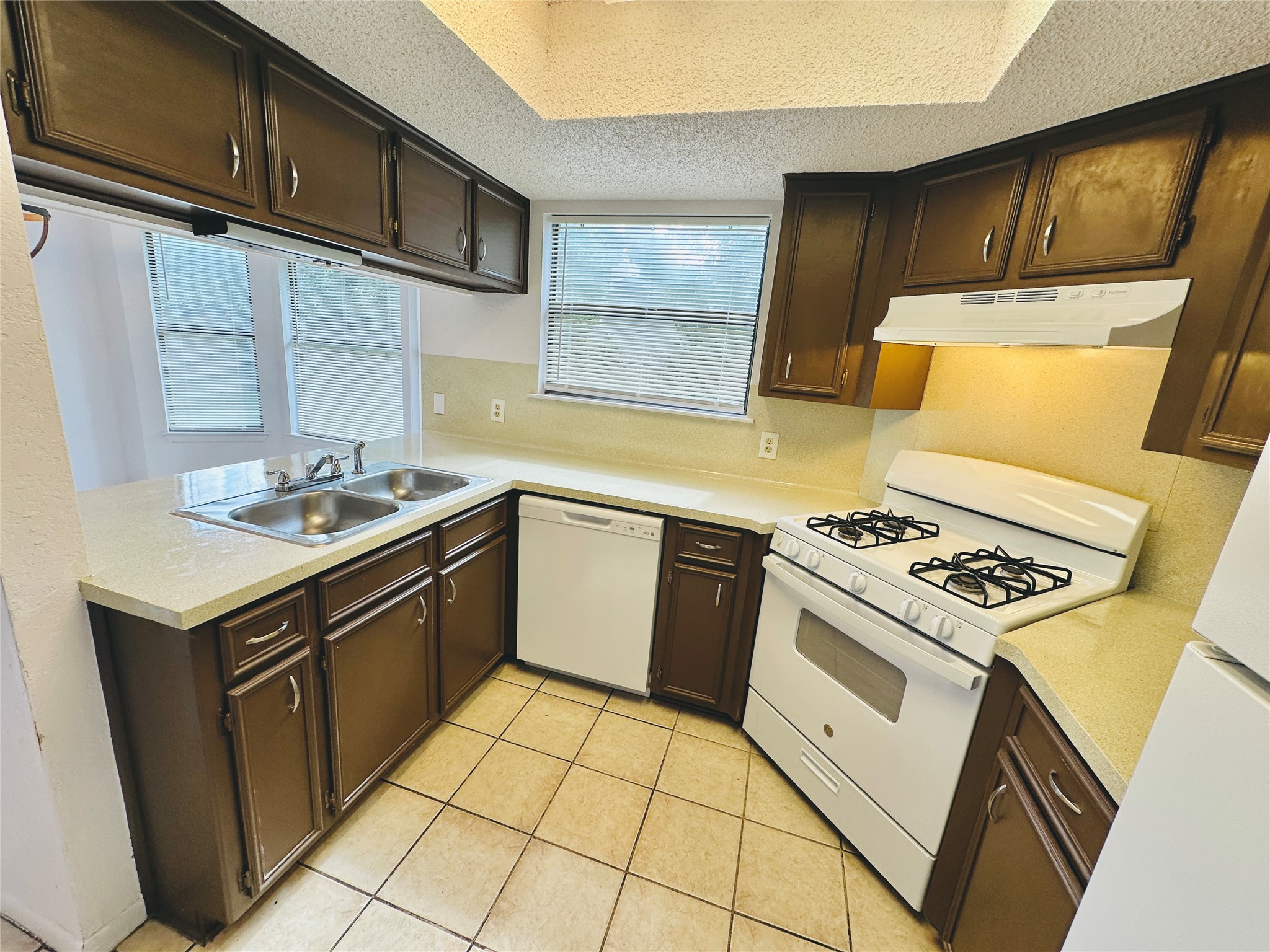 1002 Ridgemont Street Round Rock, TX 78664 - Photo 13 of 30 Kitchen featuring white appliances, a textured ceiling, light countertops, light tile patterned floors, and under cabinet range hood