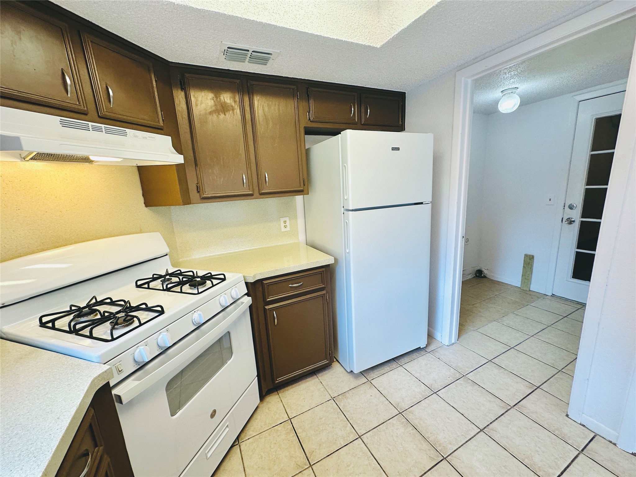 1002 Ridgemont Street Round Rock, TX 78664 - Photo 15 of 30 Kitchen featuring white appliances, a textured ceiling, light countertops, light tile patterned floors, and under cabinet range hood