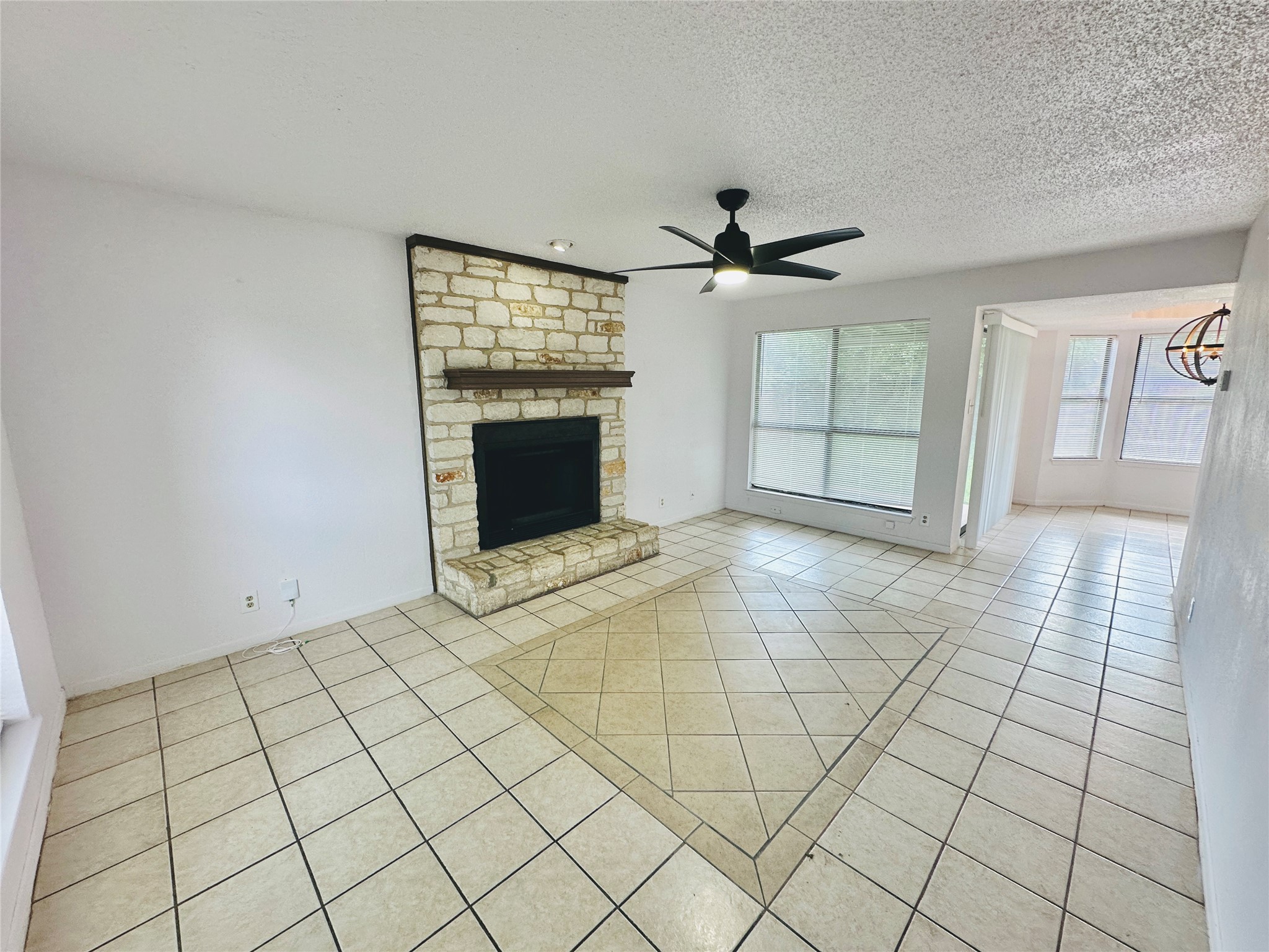 1002 Ridgemont Street Round Rock, TX 78664 - Photo 6 of 30 Unfurnished living room with light tile patterned floors, a stone fireplace, ceiling fan, and a textured ceiling