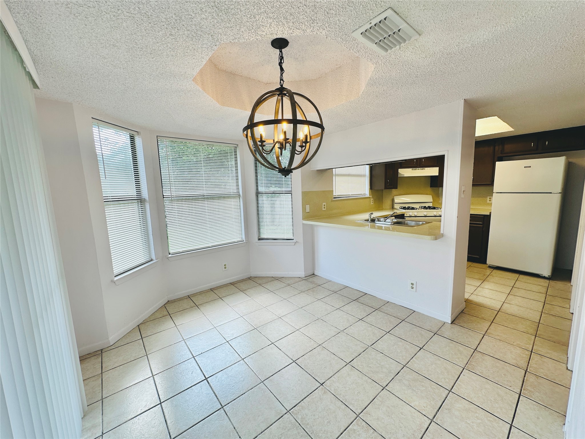 1002 Ridgemont Street Round Rock, TX 78664 - Photo 10 of 30 Kitchen featuring a textured ceiling, white appliances, light tile patterned floors, plenty of natural light, and a chandelier