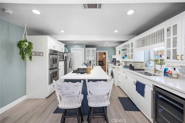 a kitchen with stainless steel appliances kitchen island granite countertop a refrigerator a stove a sink dishwasher and white cabinets with wooden floor