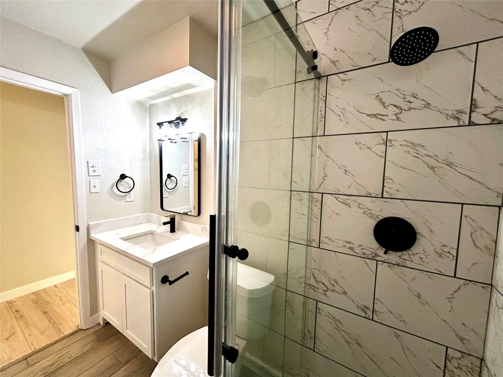 1005 West Martin Luther King Jr Boulevard Austin, TX 78701 - Photo 21 of 31 Full bathroom featuring a stall shower, vanity, a textured wall, and wood finished floors