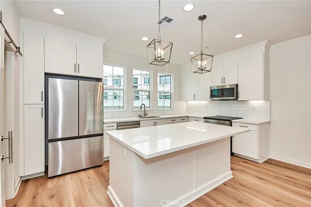 a kitchen with stainless steel appliances granite countertop a refrigerator a sink dishwasher a kitchen island with wooden floor and cabinets