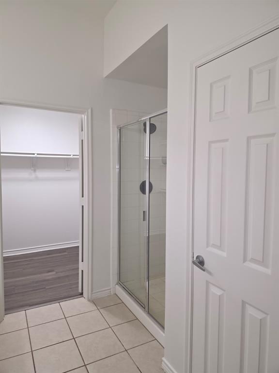 8047 New Kent Road Frisco, TX 75035 - Photo 24 of 27 Glass-enclosed shower with subway tile surround, neutral tile flooring, and a walk-in closet with wood-finish flooring and built-in shelving