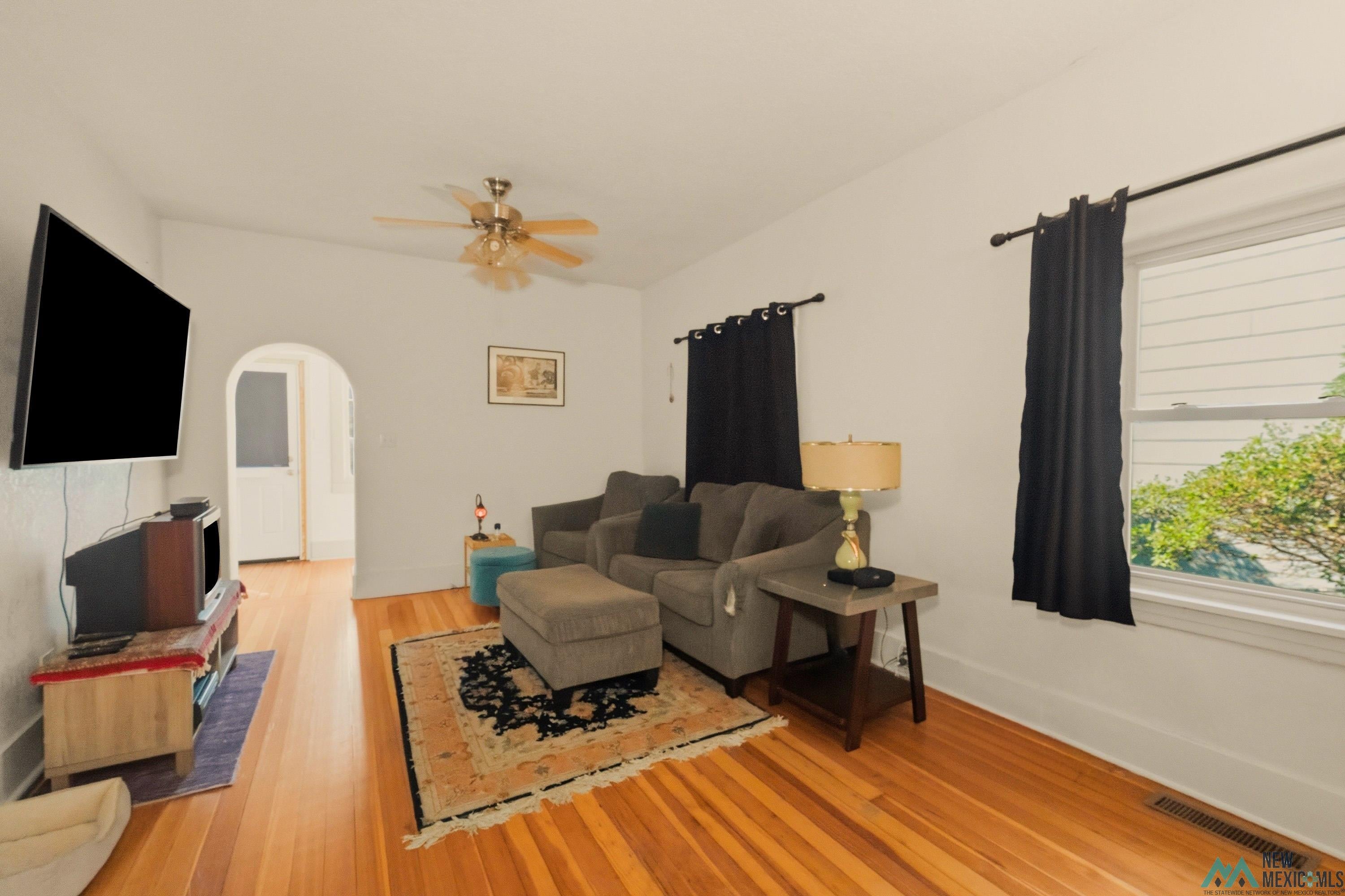 1026 South 5th Street Raton, NM 87740 - Photo 4 of 33 Living area with wood-finish flooring, a ceiling fan, and an arched doorway leading to an interior space