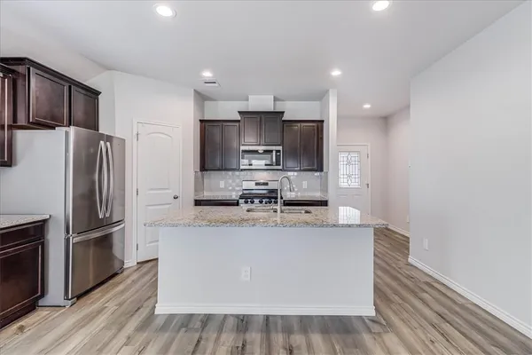 a large kitchen with stainless steel appliances granite countertop a refrigerator a stove a sink and a oven with wooden floor