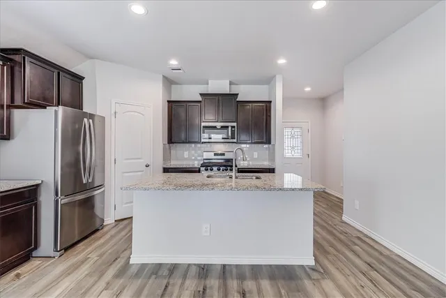 a large kitchen with stainless steel appliances granite countertop a refrigerator a stove a sink and a oven with wooden floor