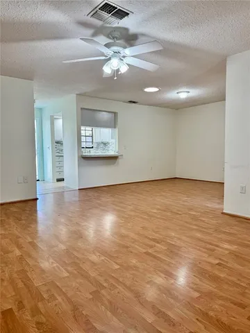 an empty room with wooden floor chandelier fan and windows