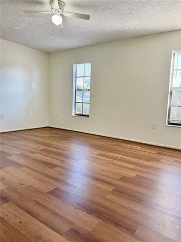 an empty room with wooden floor fan and windows