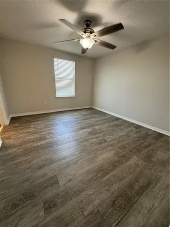 an empty room with wooden floor chandelier fan and windows