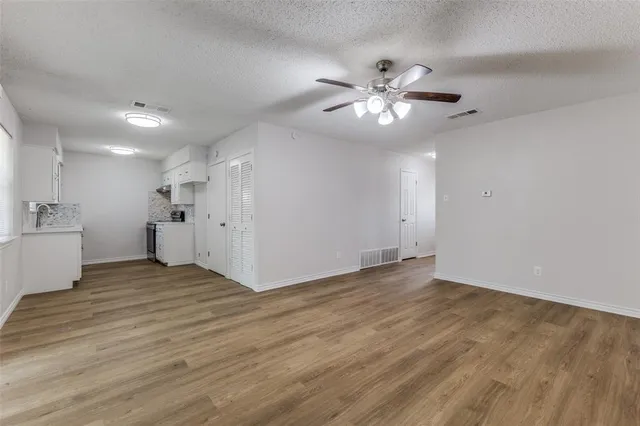 a view of an empty room with chandelier fan and wooden floor