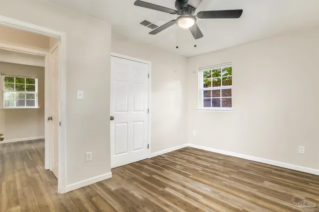 an empty room with wooden floor closet and windows