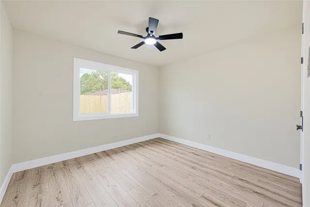 an empty room with wooden floor fan and windows