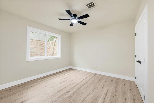 an empty room with wooden floor ceiling fan and windows