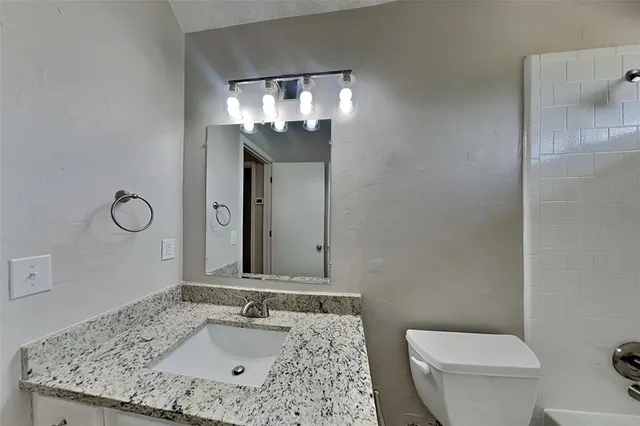 a bathroom with a granite countertop sink a toilet and a mirror