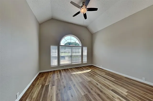 an empty room with wooden floor fan and windows