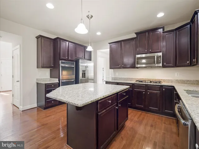 a kitchen with kitchen island granite countertop wooden cabinets a stove a oven and a refrigerator with wooden floor