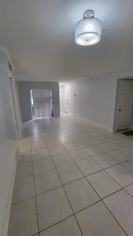 a view of an empty room with a chandelier fan and kitchen view