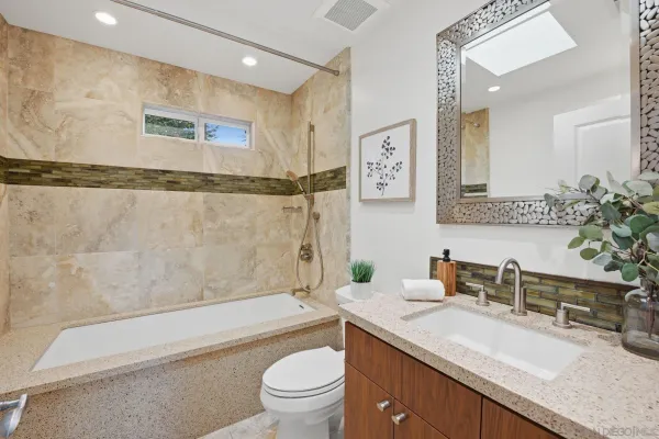 a bathroom with a granite countertop sink a toilet a mirror a vanity a bathtub and shower