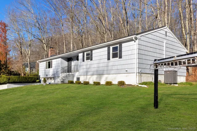 a backyard of a white house with potted plants and large trees