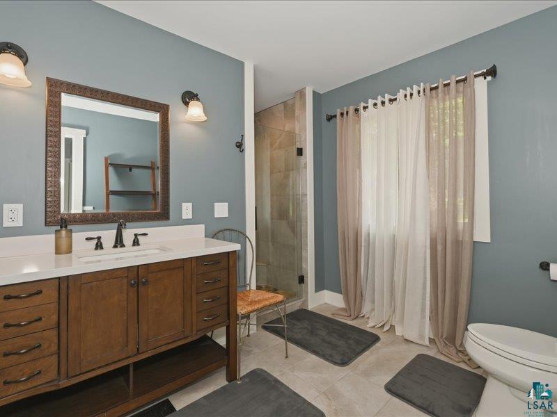 88440 Huron Street Cornucopia, WI 54827 - Photo 19 of 44 Bathroom featuring a dark wood-finish vanity with ample storage, a white countertop, and a glass-enclosed shower with tiled walls