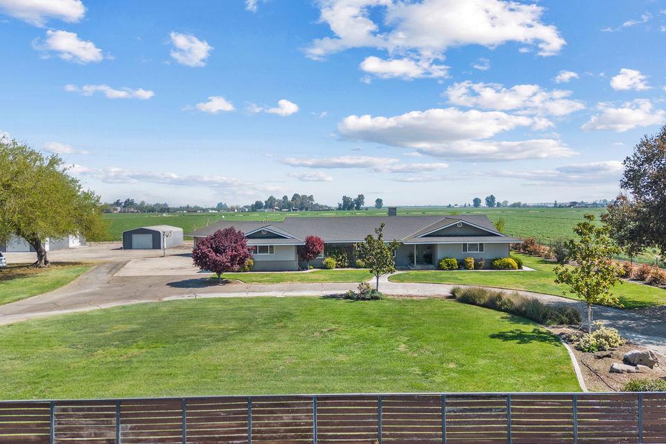 View of front facade featuring beautifully landscaped yard with a view of the countryside, two outbuildings, and a half-circle driveway.