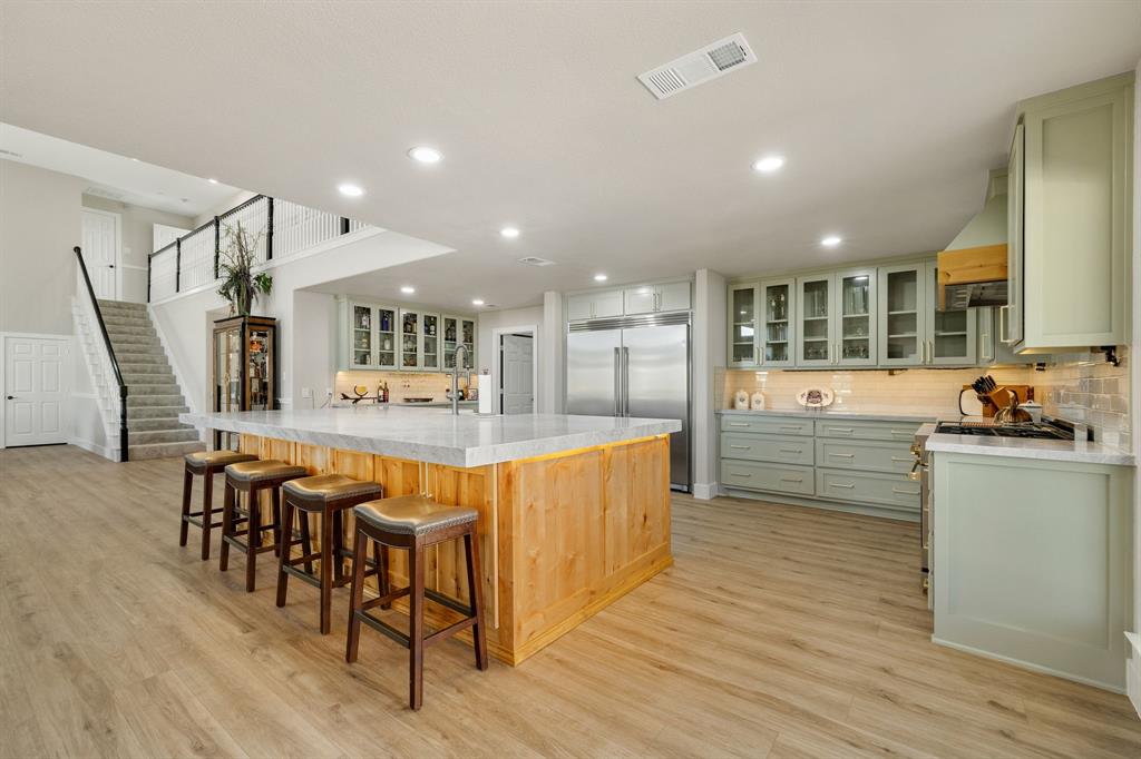12240 Wellington Road Ponder, TX 76259 - Photo 13 of 40 Expansive kitchen featuring a large wood-paneled island with seating, light green cabinetry, stainless steel appliances, and wood-finish flooring