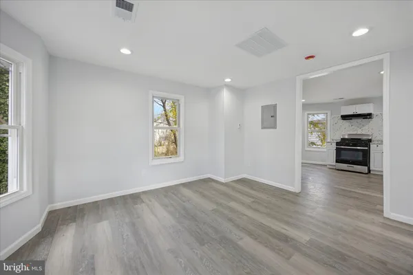 an empty room with wooden floor kitchen view and windows