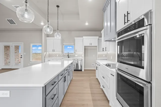 a large white kitchen with a large island oven a stove a kitchen island a sink and a chandelier