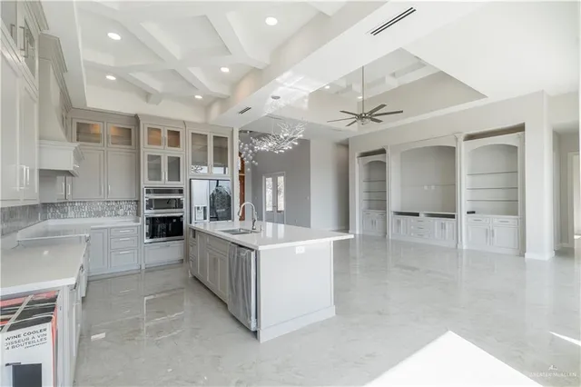 a large white kitchen with kitchen island a large counter top and stainless steel appliances