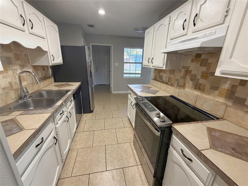 8601 Woodside Road Rowlett, TX 75088 - Photo 6 of 22 Galley kitchen featuring white cabinetry, tile countertops, a stainless steel sink, and a tile backsplash
