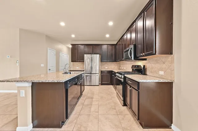 a kitchen with stainless steel appliances granite countertop a sink a stove top oven a refrigerator with island and chairs