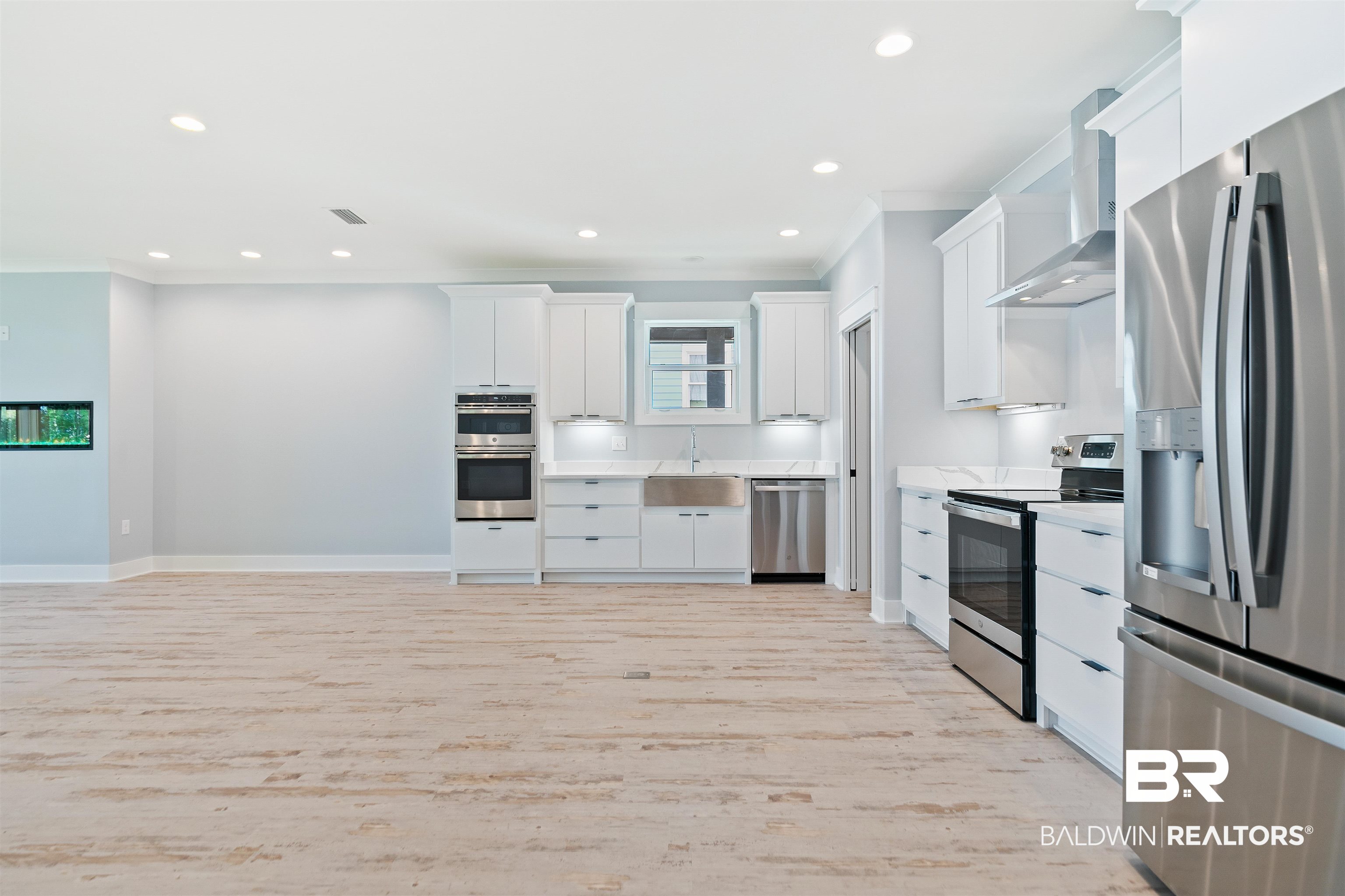 10507 County Road 1 Fairhope, AL 36532 - Photo 13 of 59 Kitchen featuring stainless steel appliances, wall chimney range hood, sink, light hardwood / wood-style floors, and white cabinetry