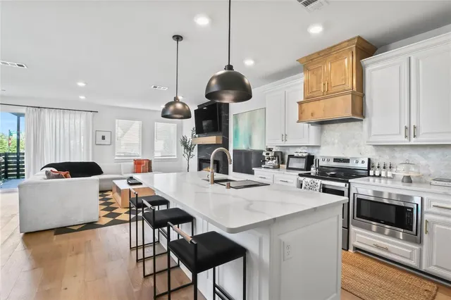 a kitchen with stainless steel appliances granite countertop a stove a refrigerator a kitchen island a sink dishwasher and white cabinets with wooden floor